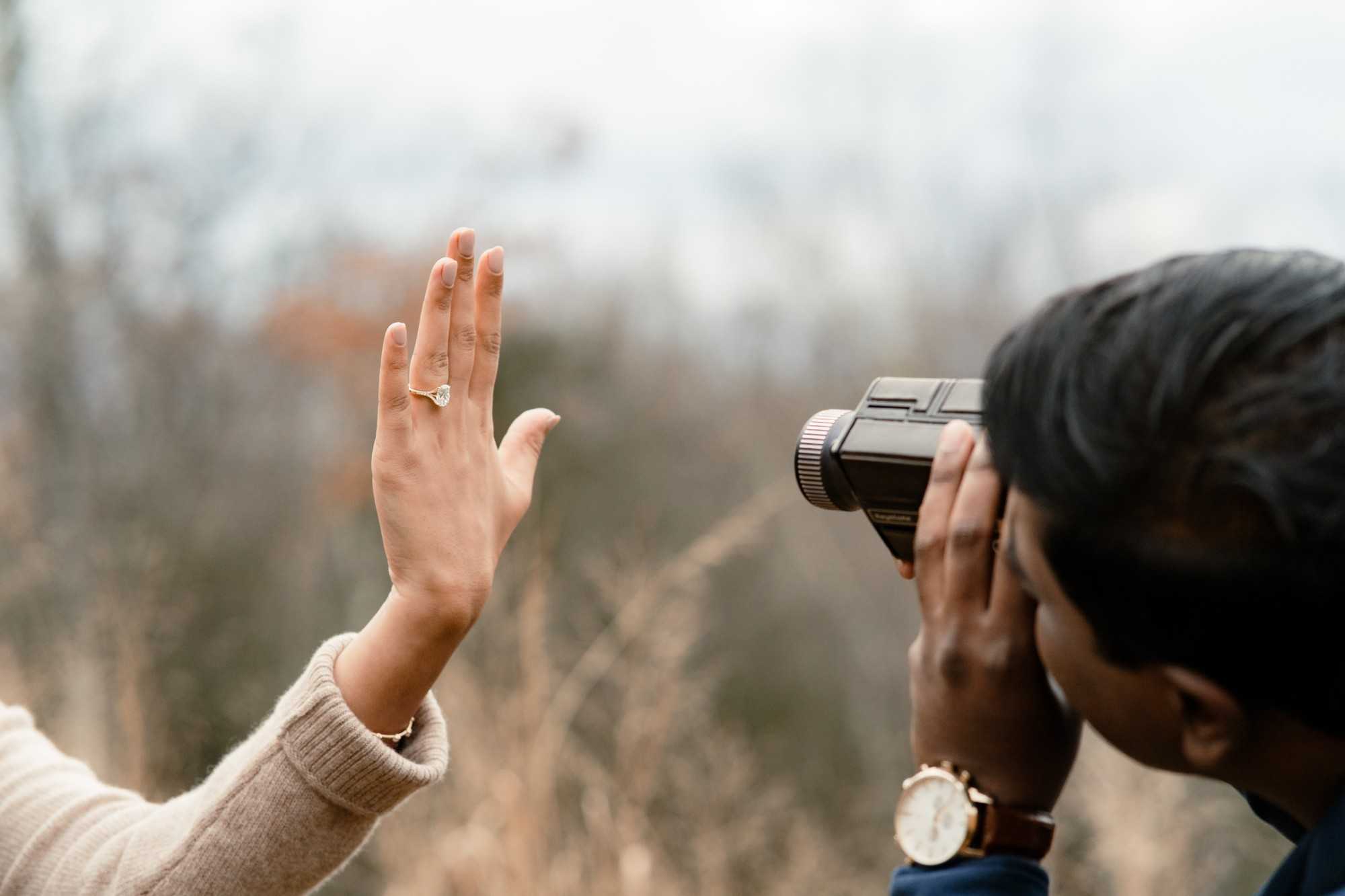 Rakesh filming with a vintage movie camera while Myra raises her hand to show her engagement ring